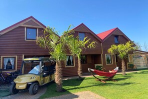 Una cabaña de madera con techo rojo, un carrito de golf y una hamaca.