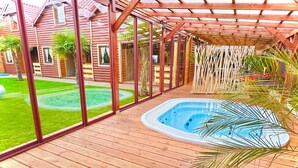 Een houten terras met een hottub en uitzicht op een huis met grote ramen.