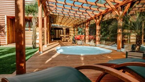 Een houten terras met een jacuzzi, lounge stoelen en een pergola.