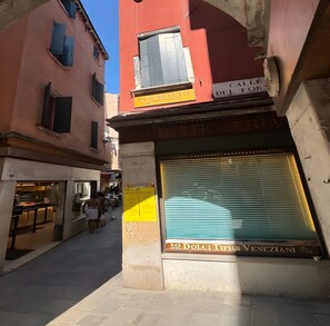 Uma rua estreita com lojas fechadas, incluindo uma pastelaria com a janela protegida por uma persiana.