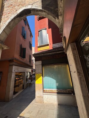 Eine Stadtstraße mit einem geschlossenen Geschäft, einem Schild für 'Dolci Tipici Veneziani' und einem steinernen Bogen.