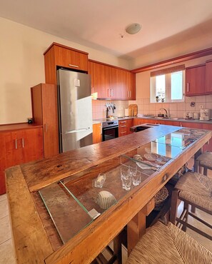 Eine Küche mit Holzausstattung, einem Edelstahlkühlschrank, einer Kochinsel mit Glasplatte und einem eingebauten Backofen.