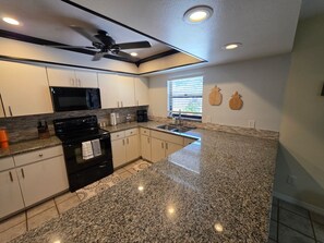 A kitchen with granite countertops, a black stove, white cabinets, a ceiling fan, and a window with blinds. - Live your best Florida life! 
Charming 3 bedroom in The Chain of Lakes region. (Winter Haven)