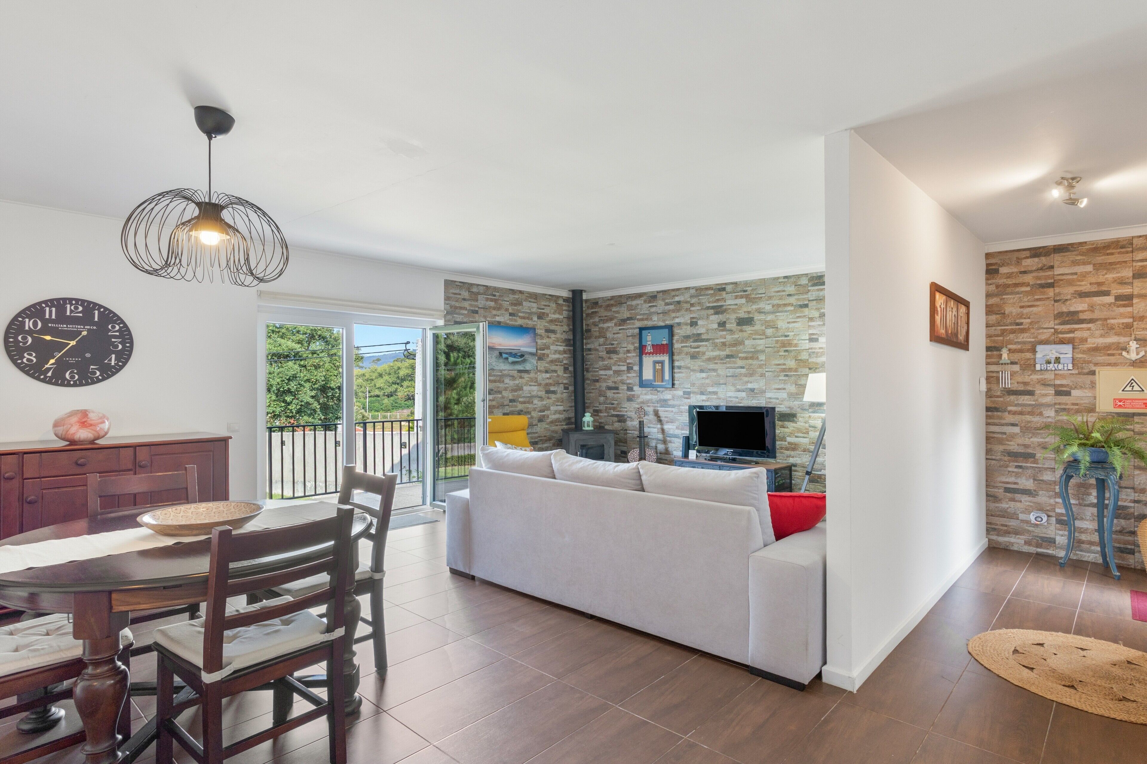 Un salon moderne comprenant un canapé, un coin repas avec une table et des chaises, une cheminée et une grande fenêtre donnant sur un paysage verdoyant.