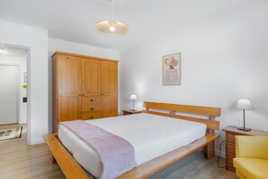 Ein Schlafzimmer mit Bett, Holzschrank, Nachttischlampen und Wandbild.