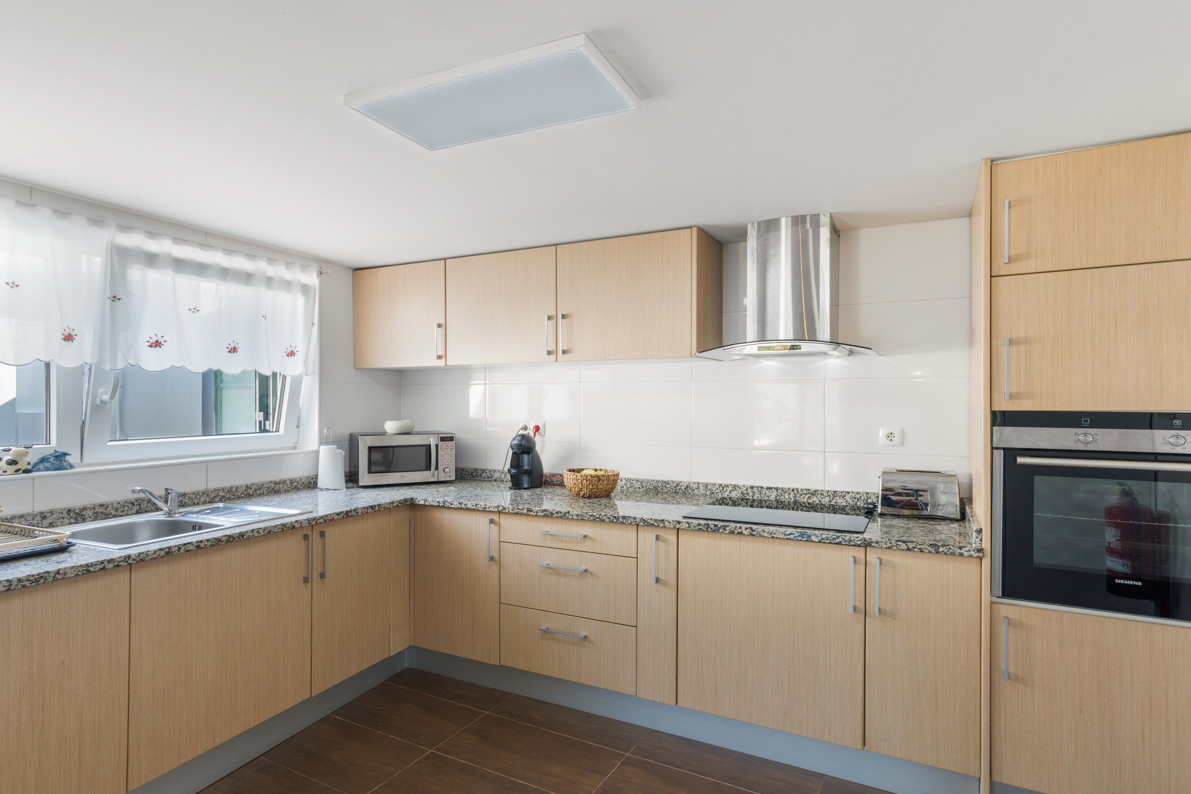 A modern kitchen with wooden cabinets, a stainless steel range hood, a microwave, a toaster, and a Siemens oven.