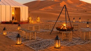 Un campamento en el desierto con una tienda, faroles y un hogar.
