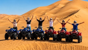 Un grupo de personas manejando vehículos todo terreno en un desierto, con dunas de arena al fondo.