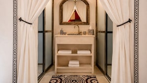 Un baño con tocador, espejo, perchero y alfombra estampada.