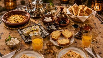 Een tafel gedekt met verschillende Marokkaanse gerechten, waaronder tagine, brood en zoetigheden, met glazen jus d'orange.