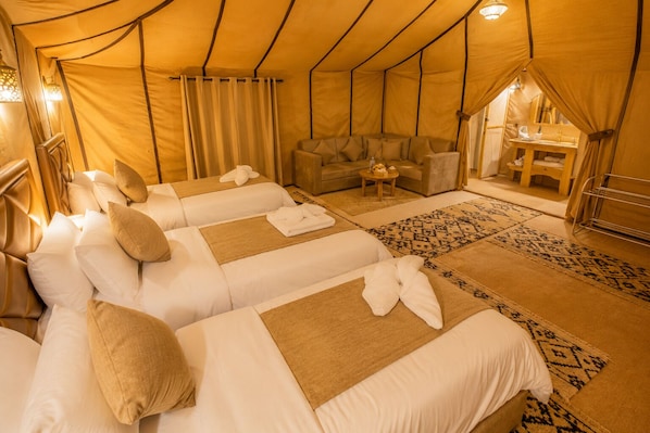 A tent-style room with three beds, a sofa, and a small table.