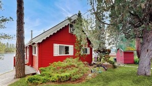 Eine rote Holzhütte mit einer kleinen Veranda, umgeben von viel Grün und einem See.