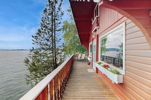 A wooden deck with a railing, a table and chairs, and a window with a view of the water.