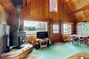 A wooden cabin interior with a fireplace, a television, and a dining area.