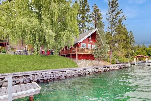 A lakeside property with a red building, a wooden dock, and a stone wall.