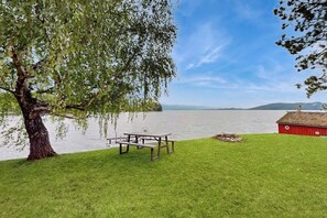 A picnic table and a red building by a lake with a clear sky.