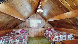 Ein gemütliches Schlafzimmer im Dachgeschoss mit zwei Betten, einem Schminktisch und einem Deckenventilator.