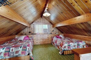 A cozy attic bedroom with two beds, a dresser, and a ceiling fan.
