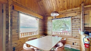 Ein Holzblock-Interieur mit Esstisch und Stühlen, großen Fenstern und einem Deckenventilator.