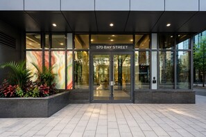 Ein moderner Gebäudeeingang mit Glasfassade, einem Schild mit der Aufschrift '570 BAY STREET' und einer begrünten Anlage mit Pflanzen.