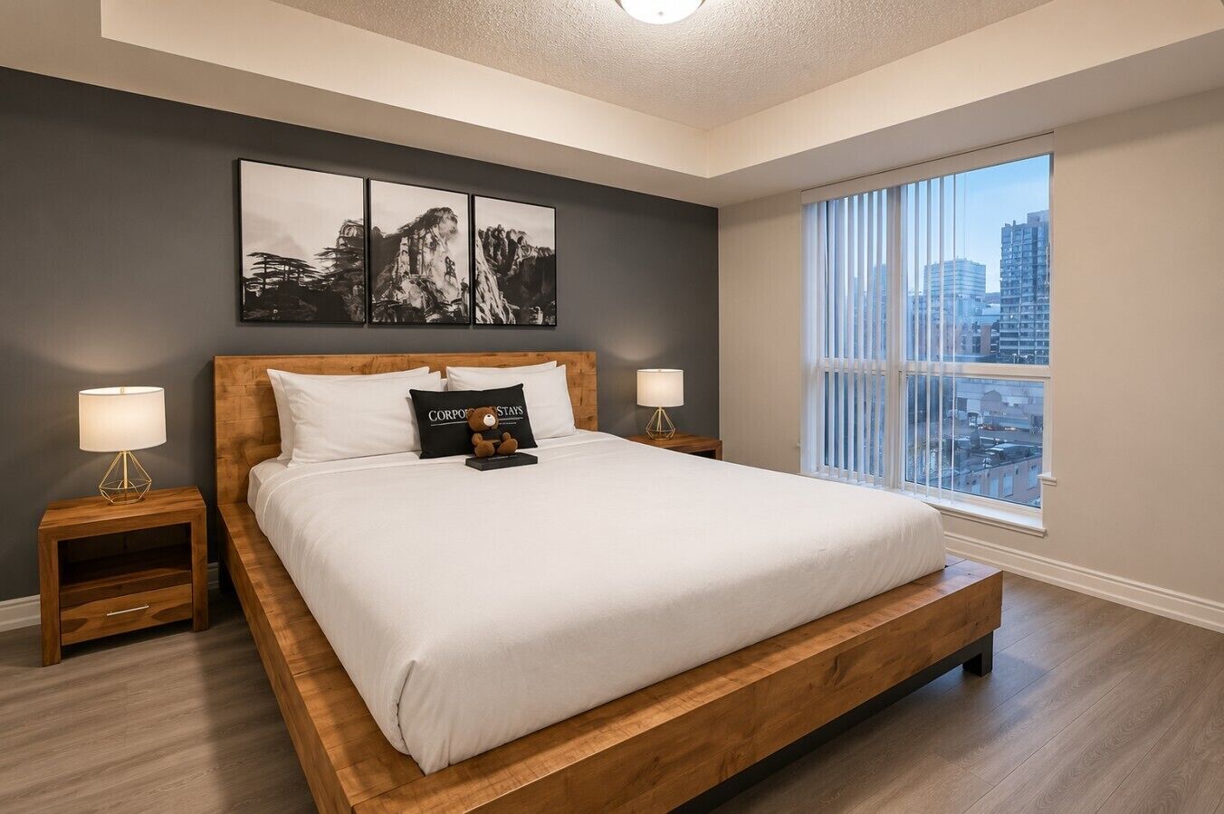 Ein modernes Schlafzimmer mit einem großen Bett, zwei Nachttischen, Blick auf die Stadt und einem gerahmten Kunstwerk über dem Bett.