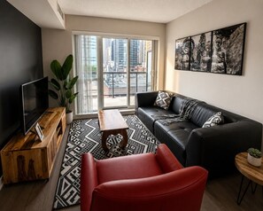 Ein modernes Wohnzimmer mit einem schwarzen Ledersofa, einem roten Sessel, einem Holztisch und einem Fernseher auf einem Holzschrank.