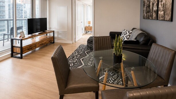 Un salon moderne avec une table à manger en verre, des canapés en cuir, un téléviseur à écran plat et une grande fenêtre donnant sur la ville.