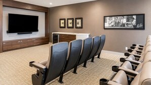 Une salle de cinéma maison équipée d’un grand téléviseur à écran plat, d’une rangée de fauteuils inclinables, d’un petit coin cuisine et de tableaux encadrés accrochés au mur.