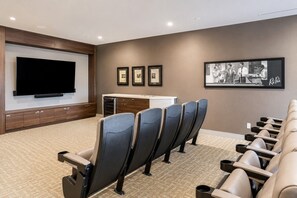 A home theater room with a large flat-screen TV, a row of reclining chairs, a small counter, and framed pictures on the wall. - Modern 1BR in Downtown | Gym, WiFi & Workspace (Toronto)