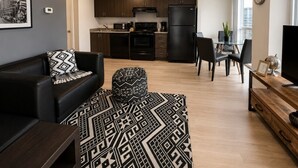 A modern living room with a black leather sofa, a patterned rug, and a dining area with a wooden table and chairs. - Bright 1BR at Motion | Prime Downtown Location (Toronto)