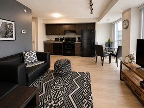Ein modernes Wohnzimmer mit einer schwarzen Ledersofa, einem gemusterten Teppich und einem Essbereich mit Holztisch und Stühlen.