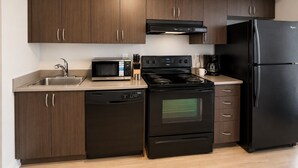 A modern kitchen with dark wood cabinets, a stainless steel sink, a microwave, a stove, a dishwasher, and a black refrigerator. - Bright 1BR at Motion | Prime Downtown Location (Toronto)