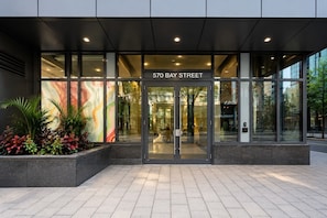 Ein moderner Gebäudeeingang mit Glasfassade, einem Schild mit der Aufschrift '570 BAY STREET' und einer begrünten Anlage mit Pflanzen.