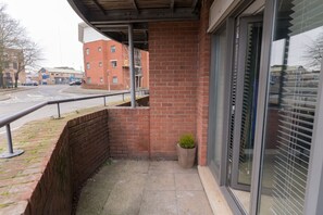 A balcony with a brick wall, a potted plant, and a view of a street with buildings. - Game Night Apartment | Walk to City Centre (Wolverhampton)