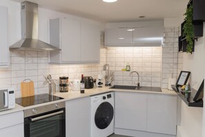 A compact kitchen with a built-in oven, a washing machine, and a stainless steel range hood. - Game Night Apartment | Walk to City Centre (Wolverhampton)