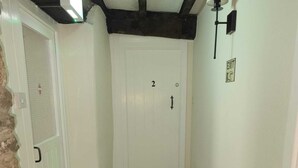 Un pasillo con una puerta blanca marcada con el número 2, un extintor y un radiador en la pared.