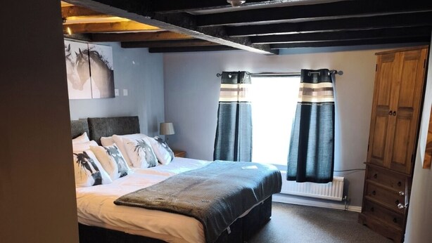 Un dormitorio con cama, mesita de noche, armario de madera y ventana con cortinas.
