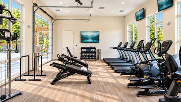 A gym with exercise equipment, large windows, and a ceiling fan.