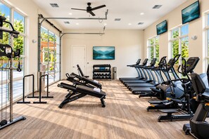 A gym with exercise equipment, large windows, and a ceiling fan.