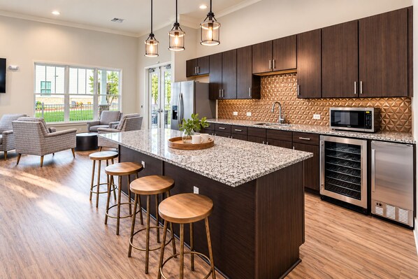 A modern kitchen with dark wood cabinets, a granite countertop, and stainless steel appliances. There are bar stools and a seating area with a view of the outdoors.