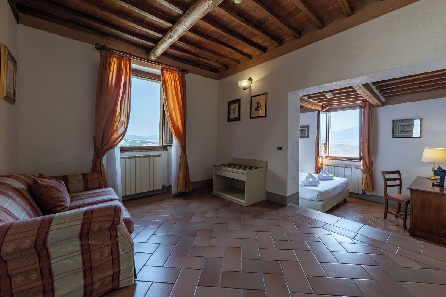 Una habitación con piso de espiga, una cama, un sofá, un escritorio y vistas a través de una ventana.