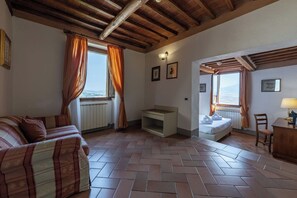 Una habitación con piso de espiga, una cama, un sofá, un escritorio y vistas a través de una ventana.
