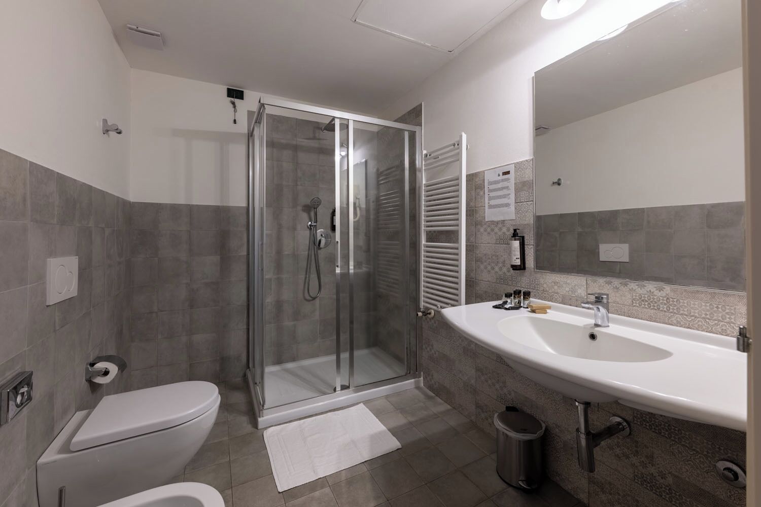 Un baño moderno con ducha de vidrio, inodoro, lavamanos con espejo y un cubo de basura.