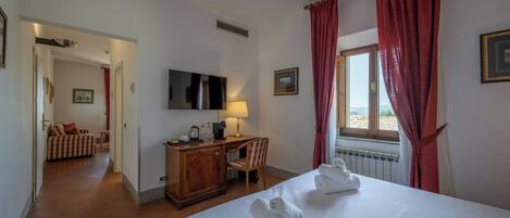 A hotel room with a bed, a desk with a lamp, a television, and a window with curtains.