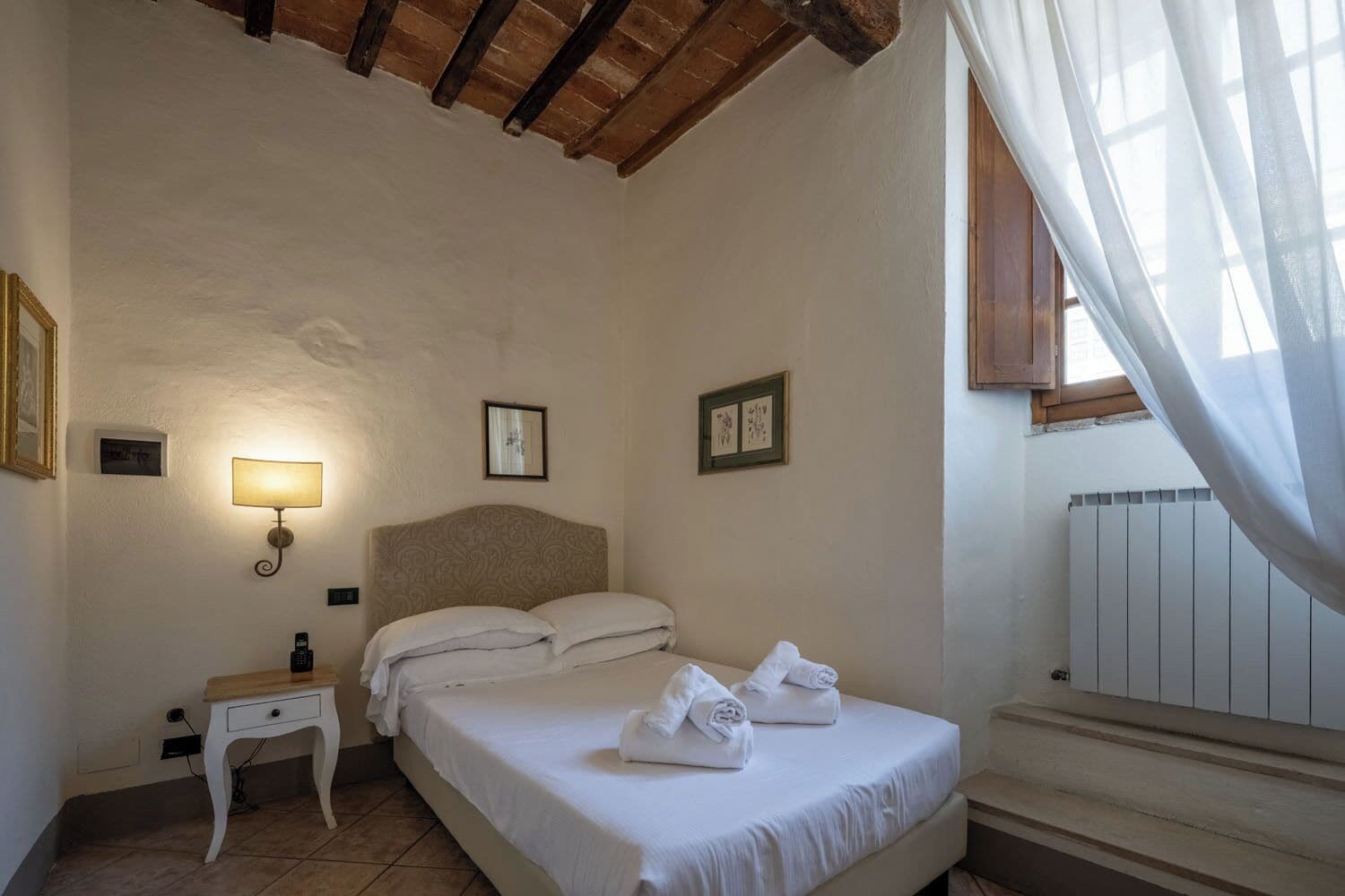 Een slaapkamer met een bed, nachtkastje, lamp en lijstjes met foto's aan de muur.