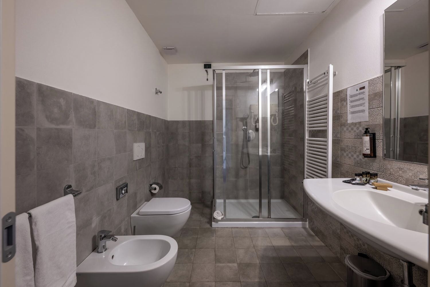 Une salle de bain moderne équipée d’un bidet, de toilettes, d’une douche et d’un grand miroir.