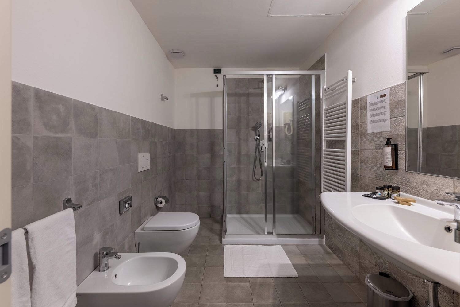 Un baño moderno con ducha, bidé y un lavamanos grande con artículos de aseo.