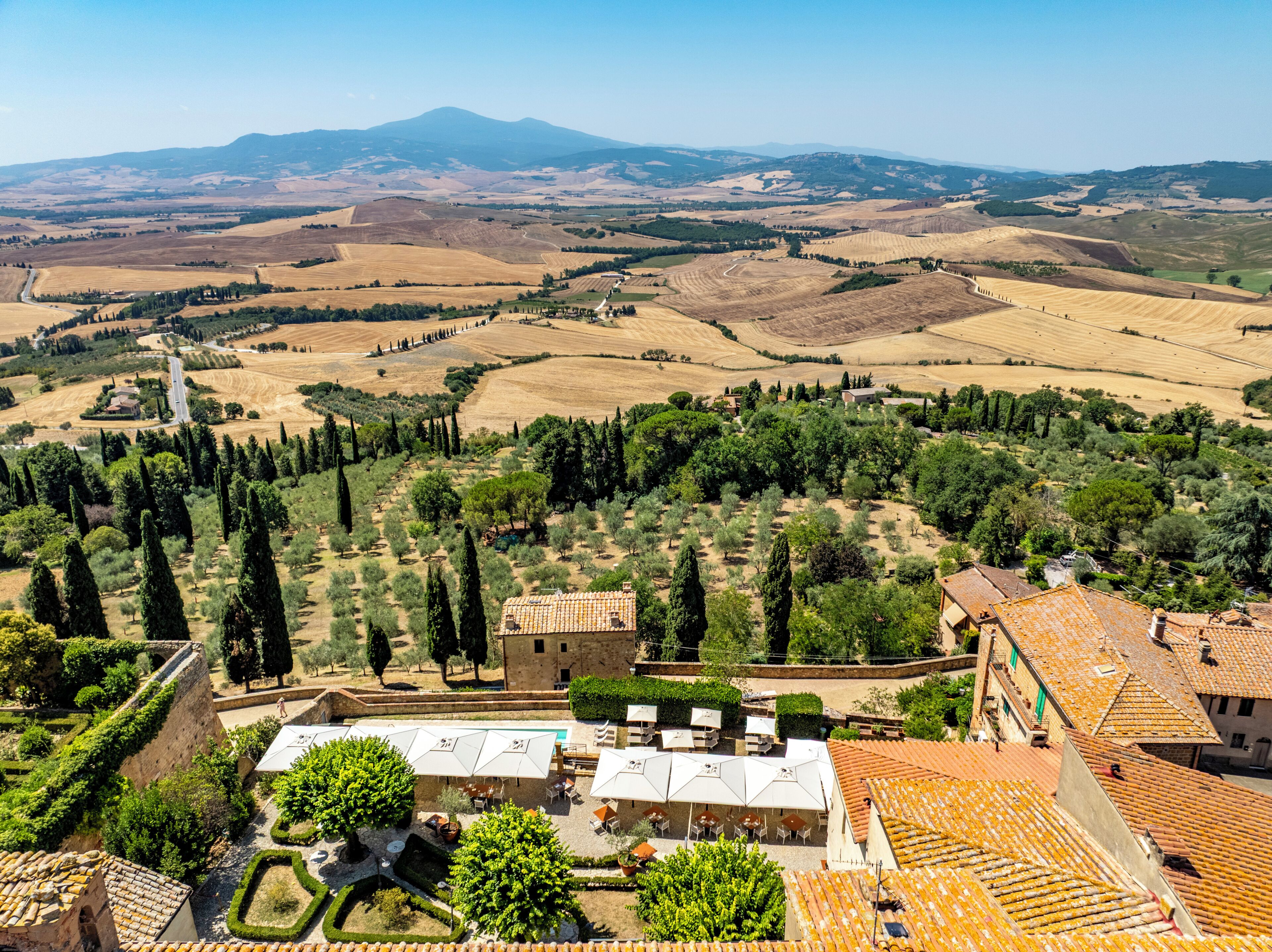 Una villa con un cortile, immersa tra uliveti e vigneti, con una montagna sullo sfondo.