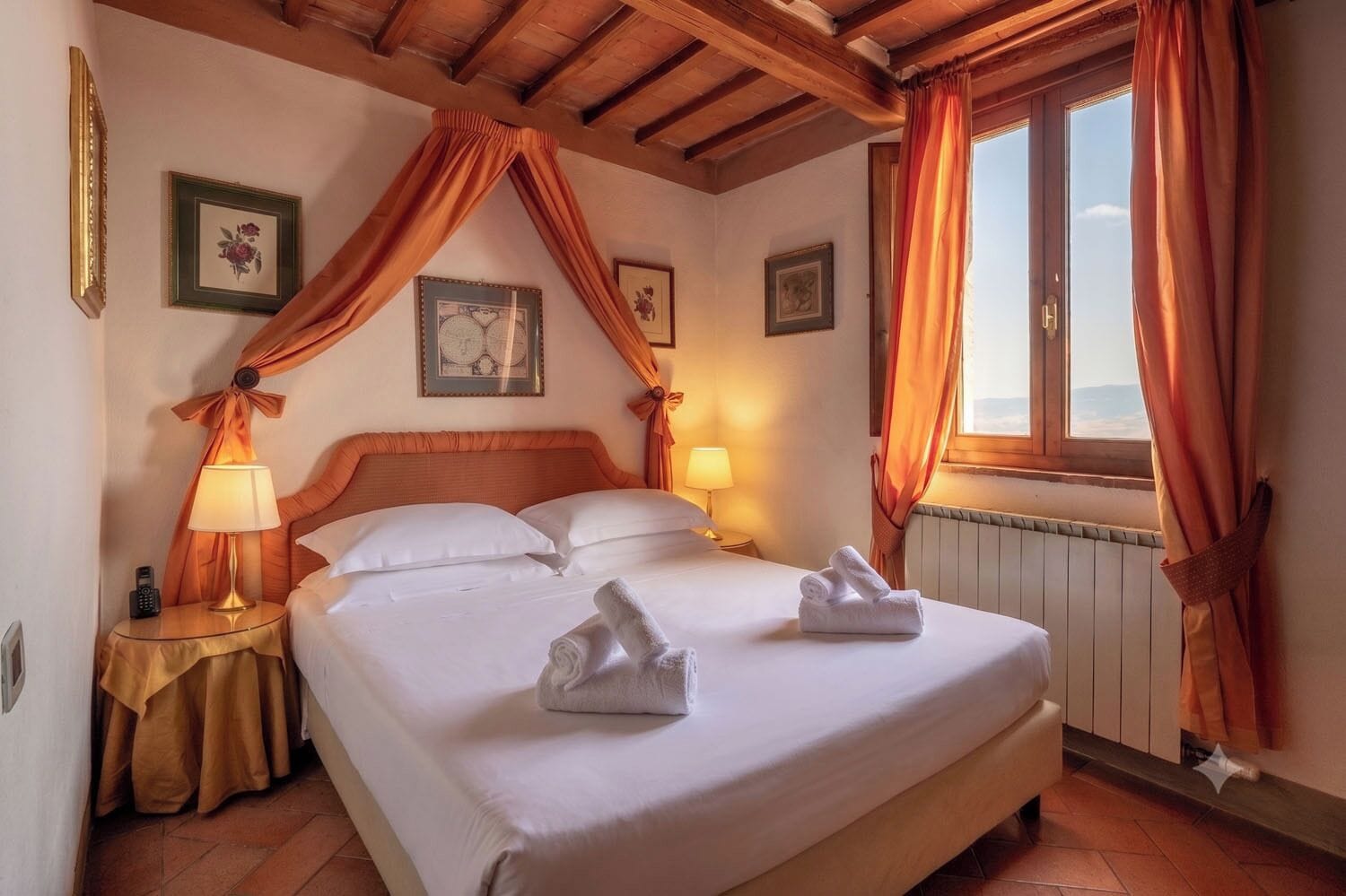 A hotel room with a bed, two bedside lamps, a window with curtains, and a radiator.