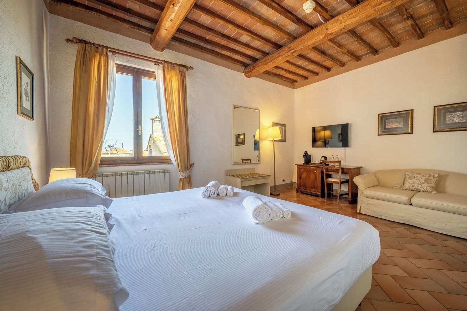 A hotel room with a large bed, a desk, a sofa, and a window with curtains.